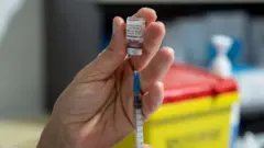 Some vaccine being drawn from a vial into a syringe