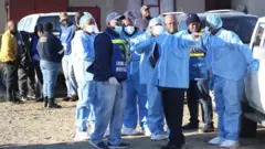 رجال الشرطة والمحققون يرتدون ملابس واقية قبل الدخول إلى حانة في بلدة شرق لندن بجنوب إفريقيا