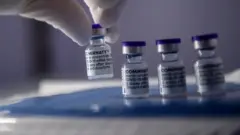 Mão usando luva segura vidrinho de vacina de RNA