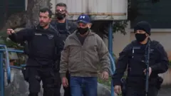 Queiroz caminha rodeado de policiais, todos de máscara