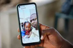 Wuri Bailo Keita, 33 anos, segura um celular mostrando uma foto dele e de sua falecida filha, Fatoumatta, que se acredita ter morrido de insuficiência renal aguda, em Banjul, em 10 de outubro de 2022. — Nos últimos 3 meses, 69 crianças morreram de insuficiência renal aguda, que se acredita ter sido causada por quatro xaropes para tosse fabricados pela empresa farmacêutica indiana Maiden Pharmaceuticals. As autoridades indianas estão investigando os xaropes fabricados pela empresa farmacêutica local após a Organização Mundial da Saúde afirmar que eles podem ser responsáveis pelas mortes das crianças na Gâmbia.