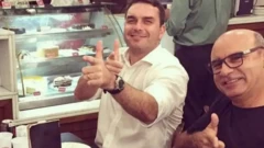 Flávio Bolsonaro posa para foto fazendo gesto de arma com as mãos ao lado de Fabrício Queiroz, que repete o gesto