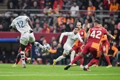 beyaz formalı iki futbolcu, sarı kırmızı formalı futbolcularla top için mücadele ediyor