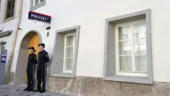 2人の警察官が、壁にドイツ語で警察の標識が掲げられた白い建物の外に立っている