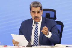 Maduro sentado, com um papel na mão e falando em um microfone