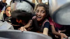 Niña luchando por recibir un plato de comida en Gaza