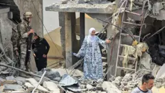 امرأة تسير وسط الركام بينما ينظر جندي لبناني في موقع مبنى سكني استهدفته غارة إسرائيلية في اليوم السابق قرب بلدة برج الشمالي، على أطراف مدينة صور، في 27 مايو/أيار 2026.