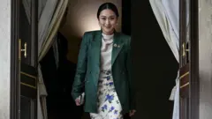 رئيسة وزراء تايلاند المقالة بايتونغتارن شيناواترا، مبتسمة أثناء الدخول من أحد الأبواب 