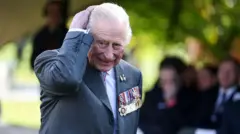 O rei Charles 3º usa blazer cinza adornado com medalhas de serviço durante a cerimônia de dedicação de um novo memorial à comunidade LGBT+ das Forças Armadas, realizada em 27 de outubro de 2025 no National Memorial Arboretum, em Alrewas, Staffordshire.