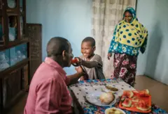Un homme recevant un aliment de la part d'un enfant alors qu'une femme voilée les regarde le sourire au lèvre