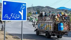 یک موتر باربری در حال عبور از لوحه کنار سرک که روی آن مسیر تورخم و لندی کوتل بازار نوشته شده است. 