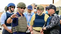 Mike Huckabee (deuxième à partir de la droite) et Steve Witkoff (à droite) se tiennent debout en gilets pare-balles, près d'un site de distribution d'aide à Gaza.