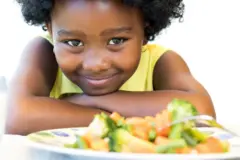 Une petite fille sourit devant un plat de légumes