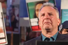 Witkoff olha para a frente com expressão séria enquanto, atrás dele, manifestantes seguram cartazes com os rostos de israelenses mantidos reféns pelo Hamas em Gaza à época.