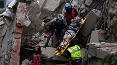 Un grupo de rescatistas saca a una mujer en una camilla de los escombros de un edificio colapsado en Caracas