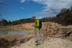 Dom anotando algo em bloco em área aberta, com areia e água