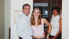 Andrés, vistiendo una camisa blanca, sonríe mientras abraza por la cintura a Virginia Giuffre, quien viste una camiseta rosada corta que deja ver su cintura descubierta. Al fondo, Ghislane Maxwell sonríe.