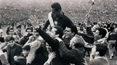 Foto em preto e branco mostra o goleiro brasileiro Gilmar dos Santos Neves sendo carregado nos ombros dos torcedores no gramado do Estádio Nacional do Chile durante as comemorações pela vitória do Brasil por 3 a 1 sobre a antiga Tchecoslováquia na final da Copa do Mundo de 1962.