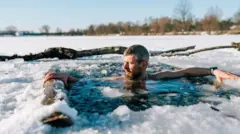 Um homem de cabelos grisalhos e barba toma banho em lago congelado durante o inverno