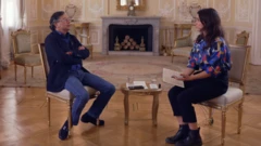 Gustavo Petro e Ione Wells estão sentados frente a frente em uma sala ornamentada, com piso de parquet e paredes em tom creme decoradas com molduras elaboradas