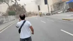 車道に立つ男性が倒壊した建物を眺めている