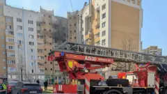 Фото девятиэтажного кирпичного дома, в котором квартиры на трех верхних этажа повреждены взрывом. Рядом стоит пожарная машина