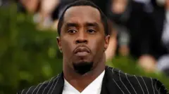 Diddy é um homem negro. Ele usa um terno preto listrado com uma camisa branca por baixo