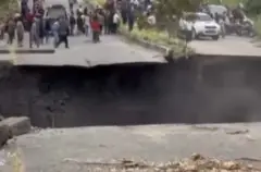 Imagem de uma cratera em uma rodovia e várias pessoas do outro lado