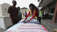 Woman setting voting paper during 2019 election in Nigeria, she dey wear red dress wit lemon jacket