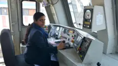 නිල් පැහැ නිල ඇඳුමක් ඇඳ දුම්රිය ධාවනයට සූදානම්ව සිටින ඉන්දියානු කාන්තා දුම්රිය රියදුරුවරියක් 