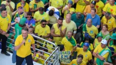 Bolsonaro falando, observado por manifestantes