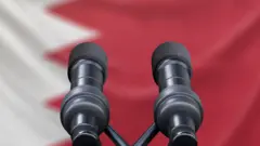 صورة تُظهر العلم البحريني وأمامه منصة وعليها ميكروفونان.