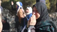 Una mujer con las manos juntas mira a la cámara mientras espera cerca de la prisión de Saydnaya, en Siria