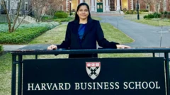 شریا میشرا پشت تابلوی مدرسه تجارت هاروارد ایستاده