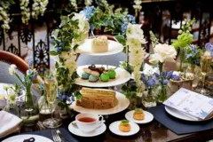 Una merienda con un puesto de pasteles, tazas de té, pasteles, flores y menús.