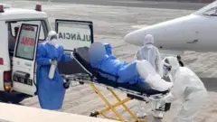 Sanitarios con equipamiento de protección especial suben a una persona en camilla a una ambulancia