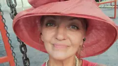 Селфи улыбающейся женщины в розовой шляпе.