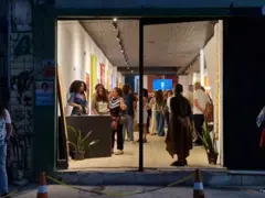 Imagem da entrada de um espaço com uma porta de vidro por onde se vê várias pessoas