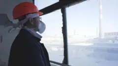 Hombre con ropa de protección mira por una ventana donde se ve la planta nuclear de Chernobyl