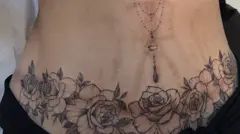 وشم من الزهور السوداء يغطي علامات ندبة خلفتها عملية جراحية وآثار تمدد الجلد في منطقة البطن.
