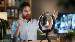 Hombre grabando un video con un teléfono y una luz circular detrás