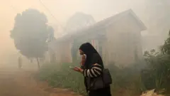Seorang warga menutup hidung saat melintas di tengah asap akibat kebakaran hutan dan lahan (karhutla) yang mendekati permukiman di Kabupaten Kubu Raya, Kalimantan Barat, 5 Agustus 2026.