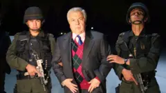 ጊልቤርቶ ሮድሪጌዝ ኦሬዉላ በፖሊስ ታጅቦ