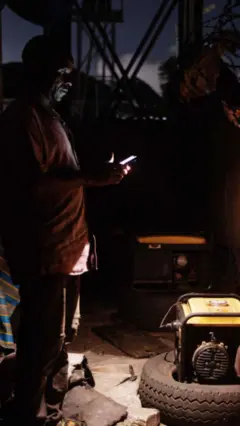 A man with phone with its torch on stands around generators
