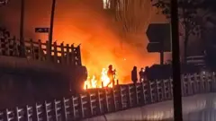 Uzbrojony członek irańskich sił bezpieczeństwa widziany przed płonącym budynkiem podczas protestu w Teheranie, 9 stycznia 2026 roku