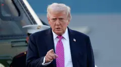 د امریکا ولسمشر ډونلډ ټرمپ په درېشۍ کې ولاړ دی چې ګلابي رنګه خالداره نېټکټايي یې اچولې او ګوته یې مخامخ په اشاره نیولې ده.