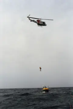 Un helicóptero se mantiene en vuelo estacionario sobre los coches en el mar, izando a dos hombres hasta un lugar seguro.