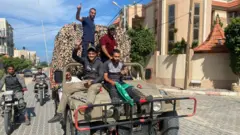 Palestinos comemoram enquanto viajam em um veículo militar israelense que foi apreendido por homens armados que invadiram áreas do sul de Israel