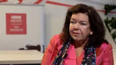 Žena tamne duge kose u roze sakou i sa cvetnim šalom gleda