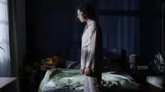 একজন নারী চোখ বন্ধ করে বিছানার পাশে দাঁড়িয়ে আছেন